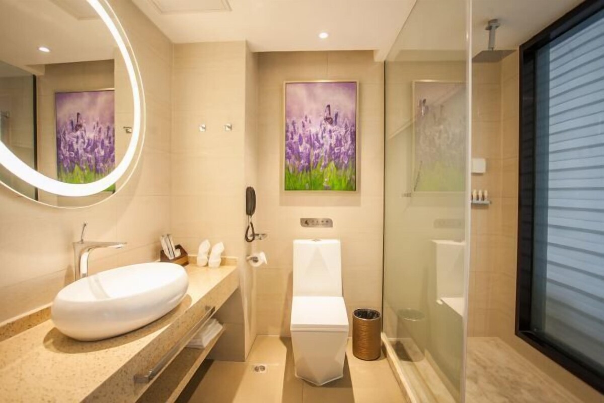 A modern bathroom with a large oval sink, a toilet, and a glass-enclosed shower. There are two framed floral paintings on the wall.