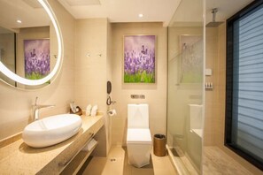 A modern bathroom with a large oval sink, a toilet, and a glass-enclosed shower. There are two framed floral paintings on the wall. - Lavande Hotel (Guilin Railway Station Mixc) (Guilin)