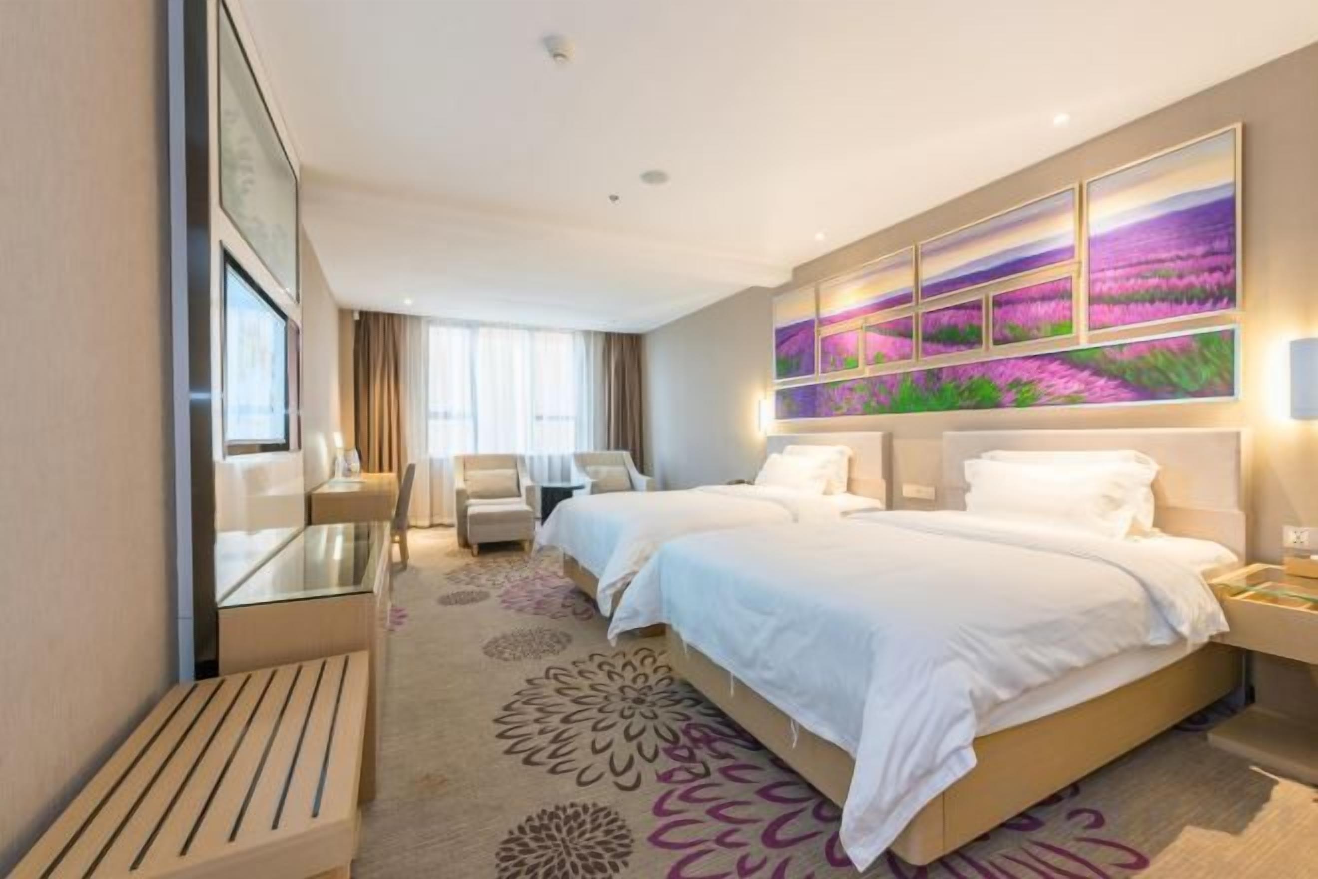 Quarto de hotel com duas camas, uma escrivaninha, uma cadeira e uma janela grande.