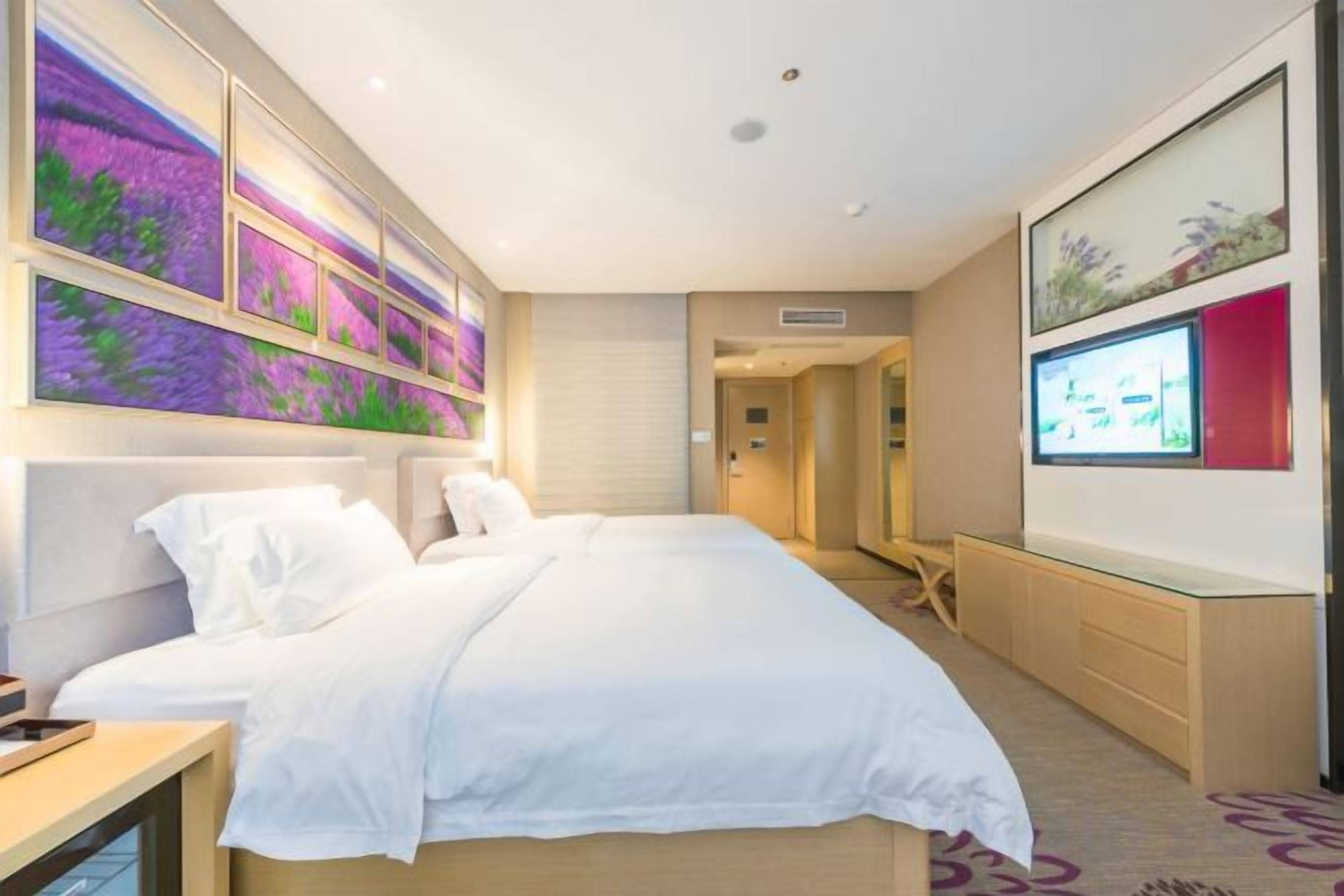 A hotel room with a large bed, a TV, and artwork on the walls.