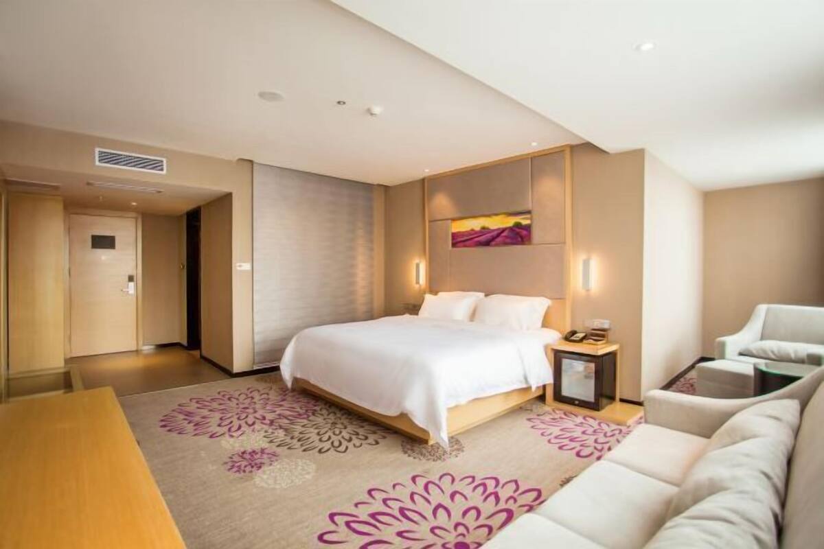 A modern hotel room with a bed, a nightstand, a sofa, and a decorative rug.