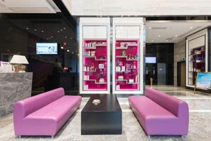 A lobby with two purple sofas, a black coffee table, and a reception desk with a TV screen. - Lavande Hotel (Guilin Railway Station Mixc) (Guilin)