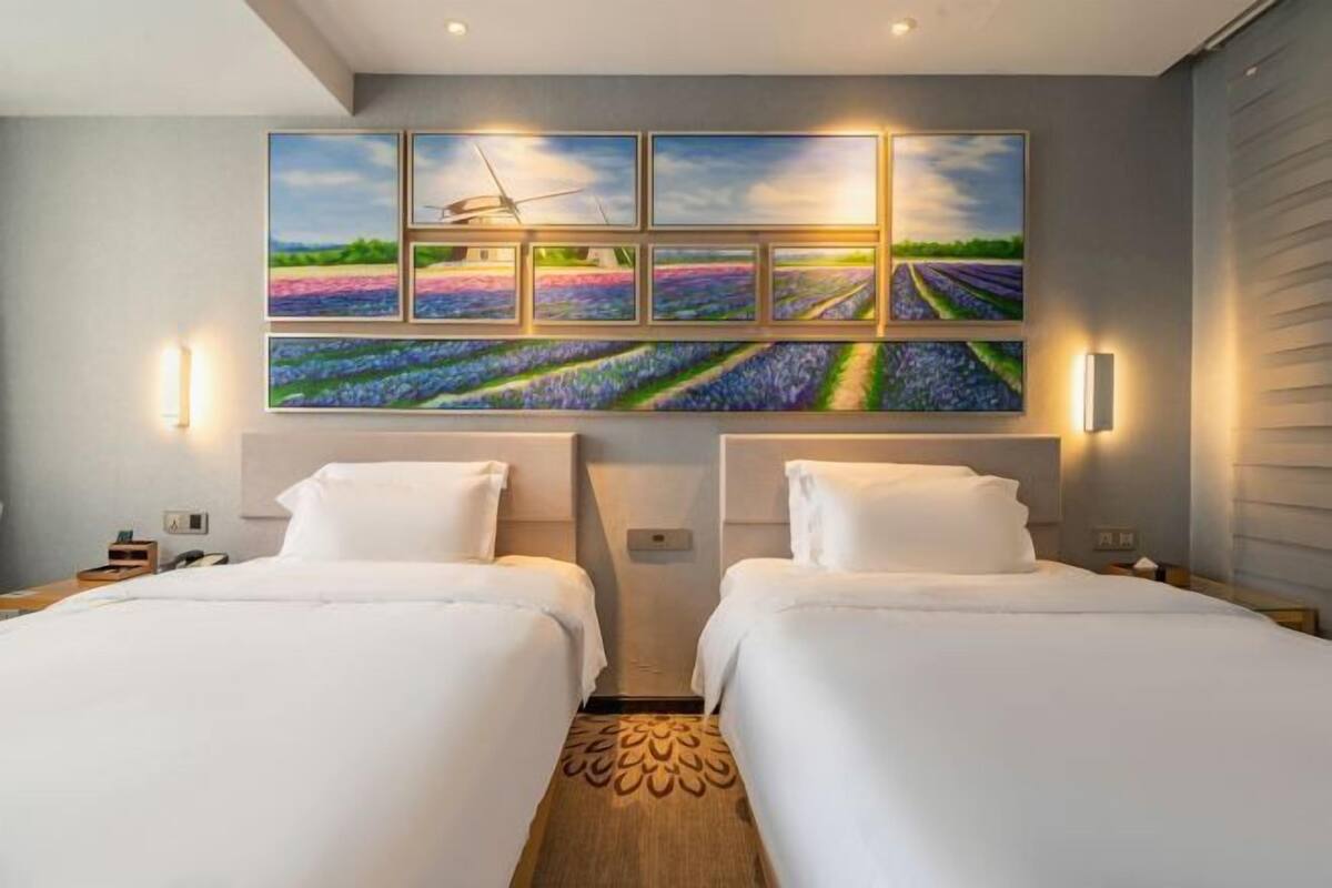 A hotel room with two beds, a large painting of lavender fields, and a wooden floor pattern.