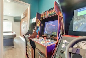 Una habitación con una máquina arcade de Mortal Kombat, una mesa de billar y una pantalla de televisión mostrando un juego.