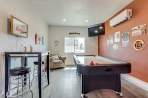 Mesa de billar con taburetes, zona de bar y letrero que indica sala de juegos.