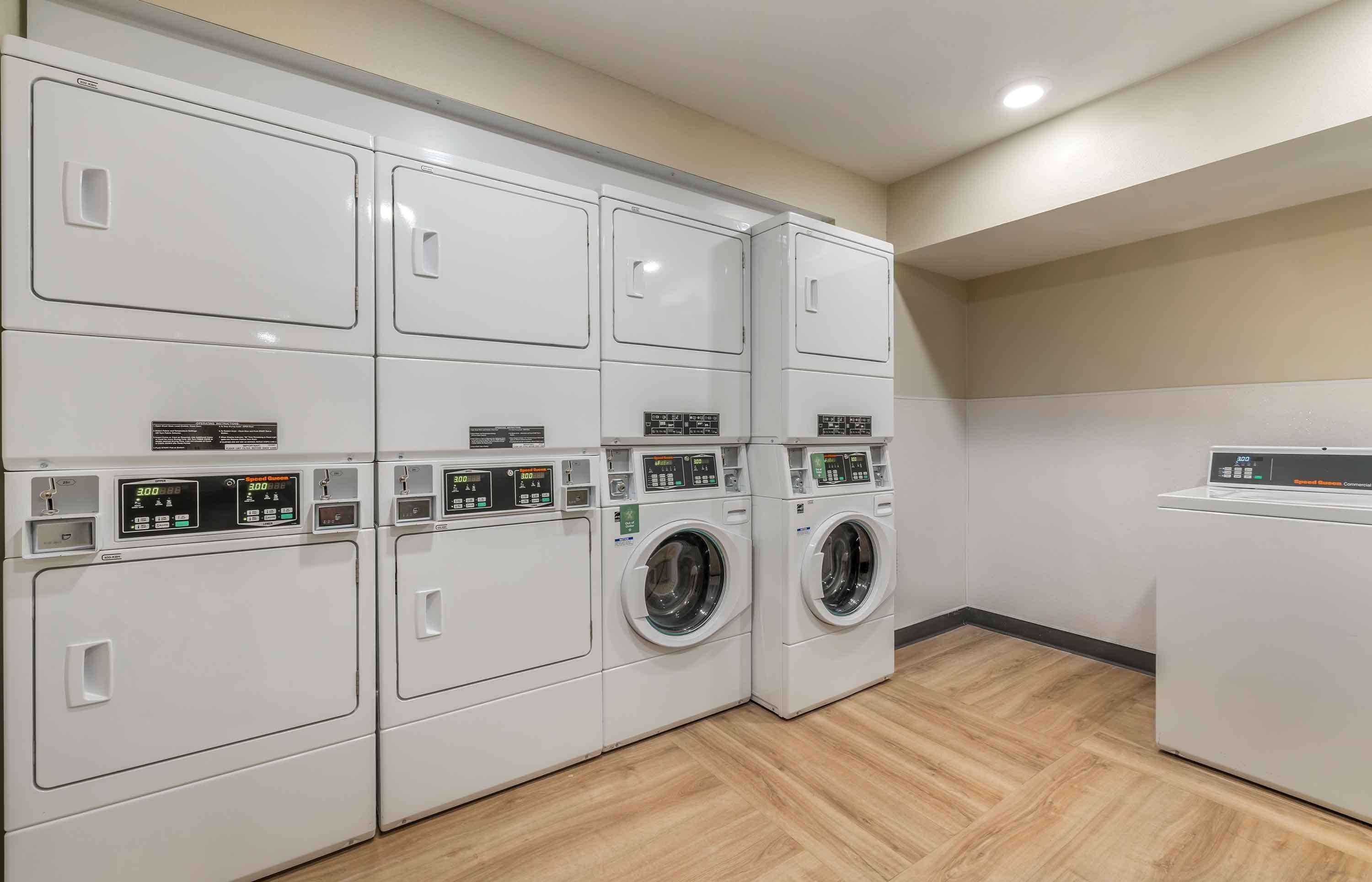 A laundry facility with multiple washing machines and dryers, a digital control panel, and a wooden floor.