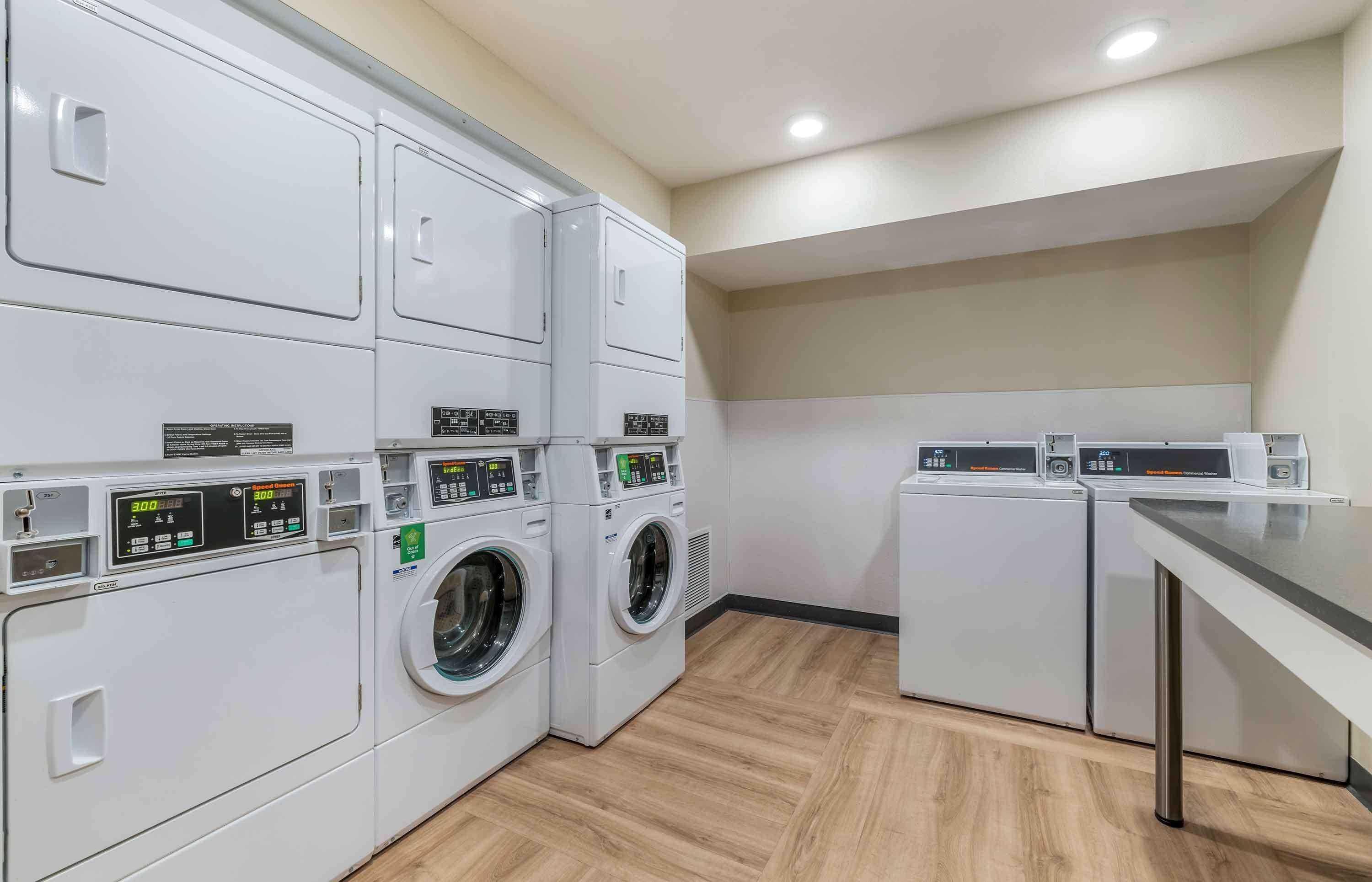 Une buanderie équipée de plusieurs machines à laver et de plusieurs sèche-linge, dotée d’un plancher en bois et présentant un design moderne.