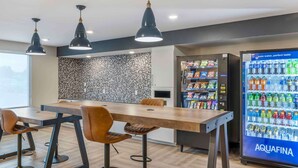 A modern dining area with a long table and bar stools, a vending machine, and a water dispenser. - Extended Stay America Premier Suites - San Diego - San Marcos (San Marcos)