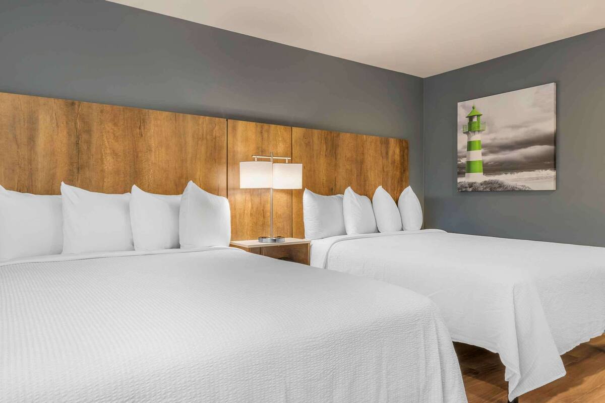 Une chambre d’hôtel avec deux lits, une tête de lit en bois, une lampe de chevet et un tableau représentant un phare.