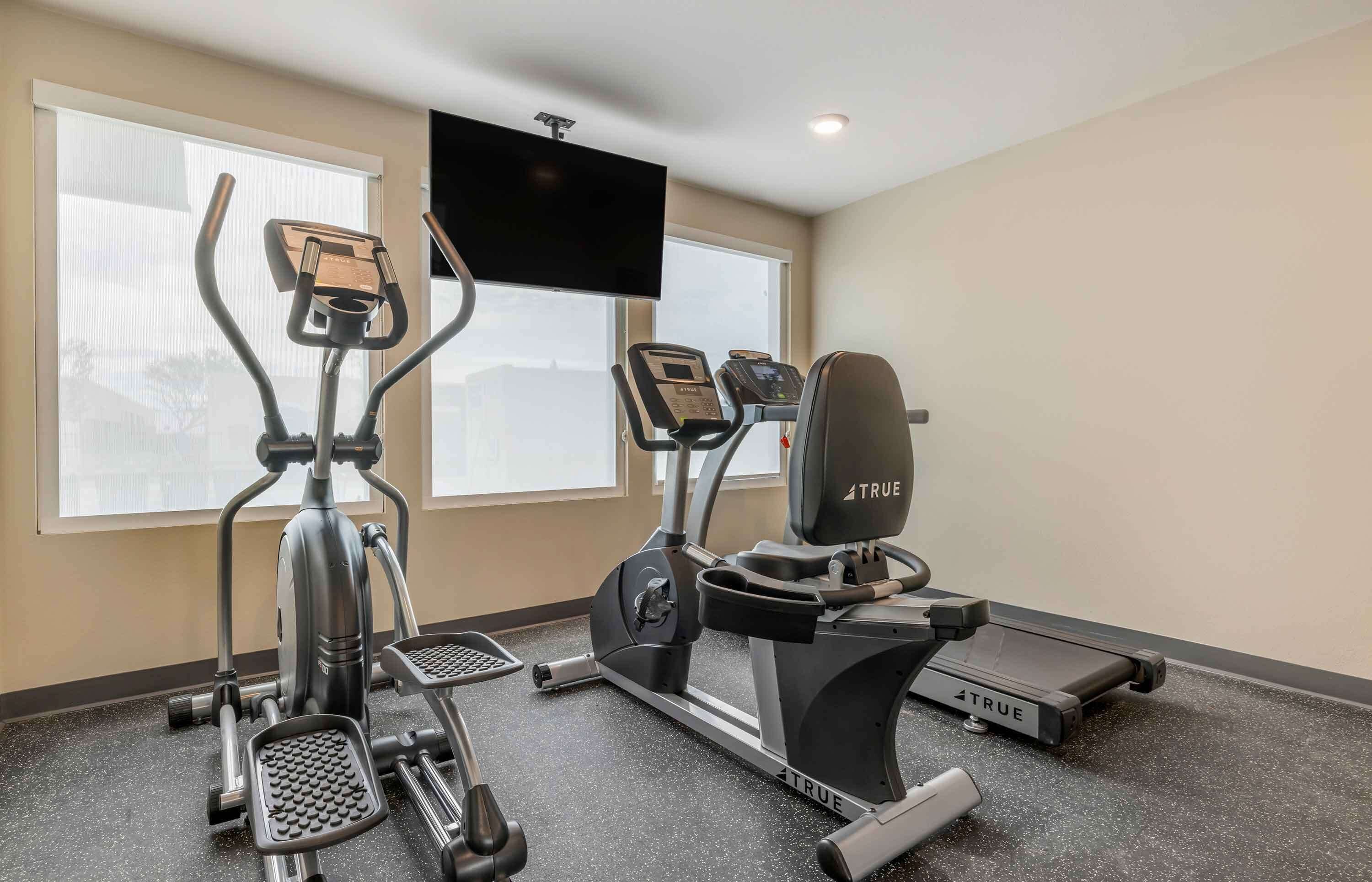 A fitness room with an elliptical, a treadmill, and a stationary bike, all branded with 'TRUE'.