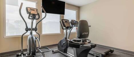 A fitness room with an elliptical, a treadmill, and a stationary bike, all branded with 'TRUE'.