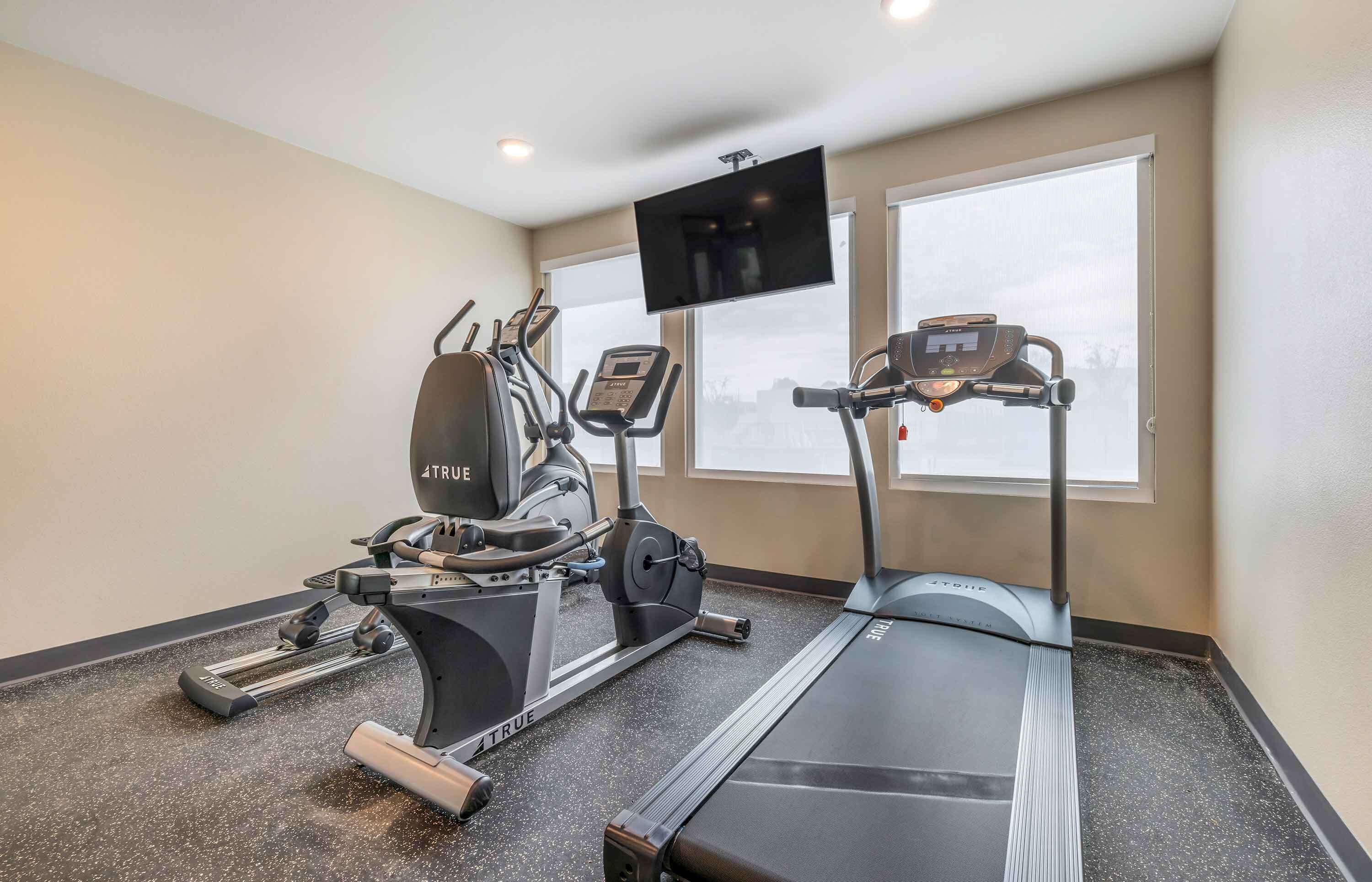 A fitness room with treadmills, elliptical machines, and a TV screen.