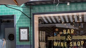 An outdoor seating area with tables and chairs, a sign indicating the establishment is a bar and wine shop, and a door with a 'We are open' sign. - Sugar Boat (Helensburgh)