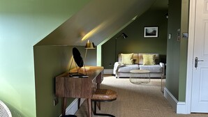 A loft bedroom with a sloped ceiling, a desk with a lamp, a chair, a sofa, and a small round table. - Sugar Boat (Helensburgh)