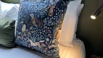 A bed with a decorative pillow featuring a bird and floral pattern, a green pillow, and a bedside lamp.