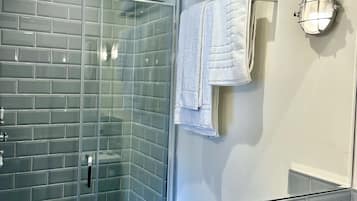 Un baño moderno con ducha de vidrio, lavamanos blanco y toallero con toallas dobladas.