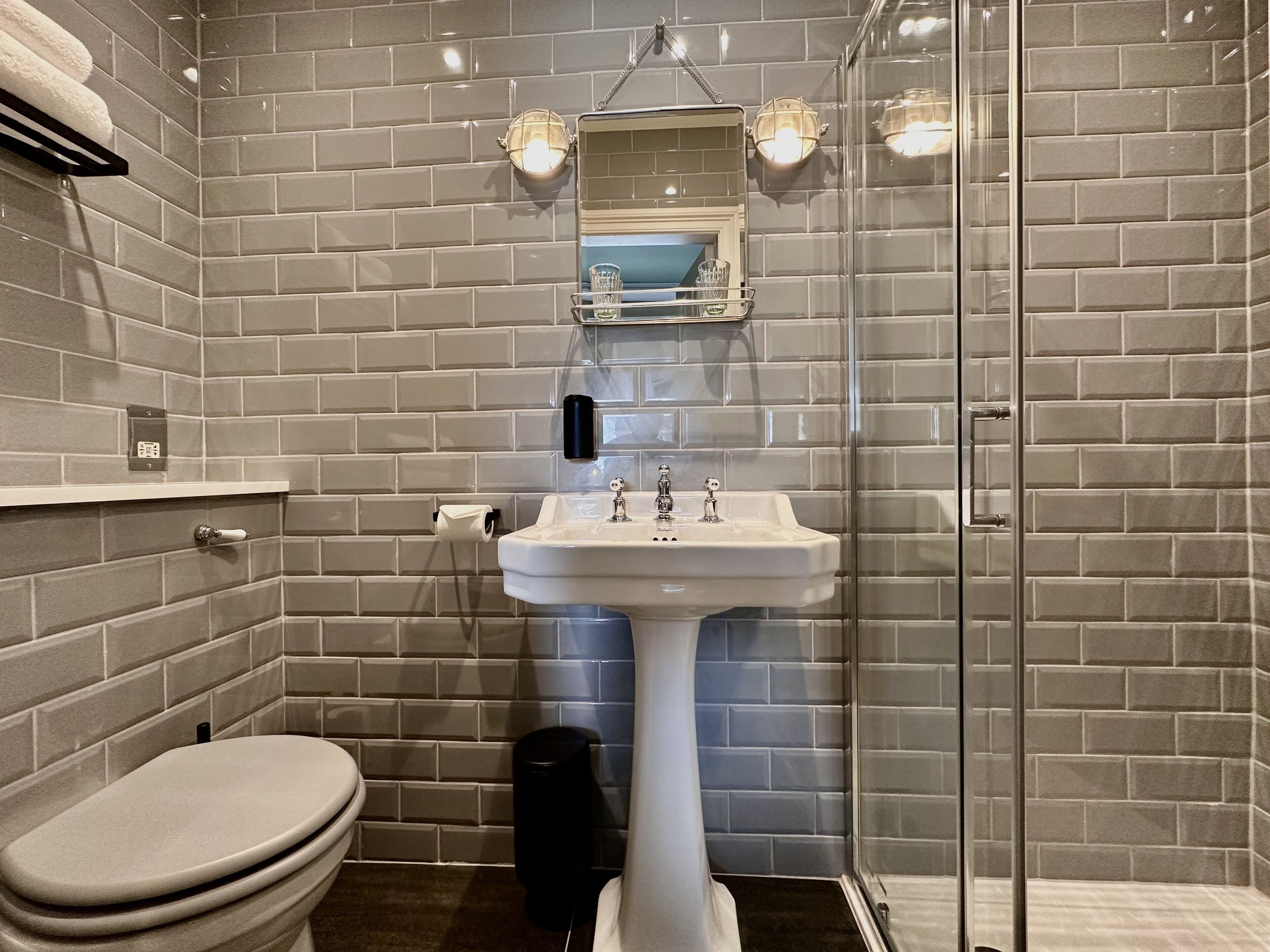A bathroom with a white pedestal sink, a glass shower enclosure, and a toilet.