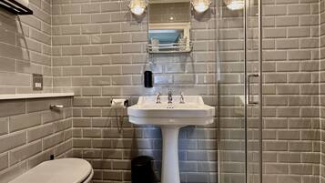 A bathroom with a white pedestal sink, a glass shower enclosure, and a toilet.