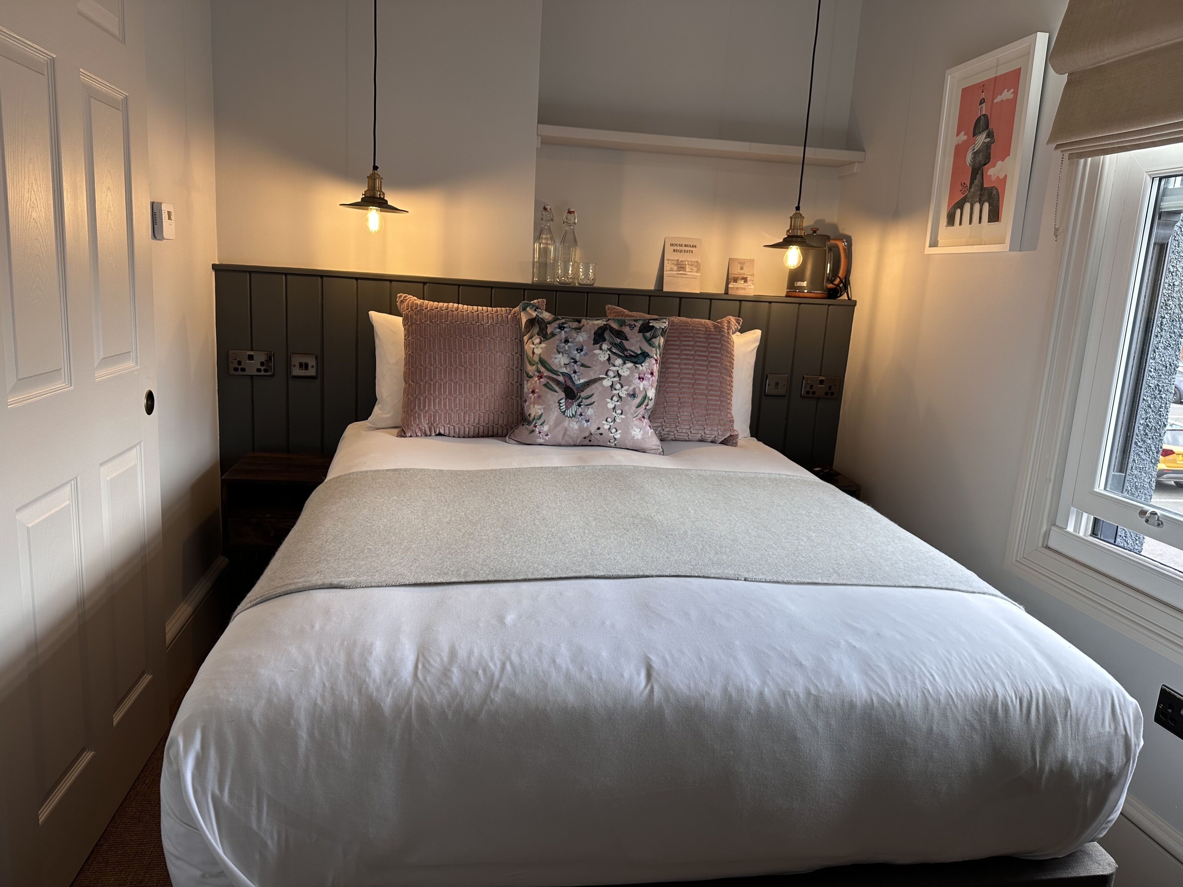 Een net opgemaakt bed met een witte deken, twee kussens en een hoofdbord met een lamp.