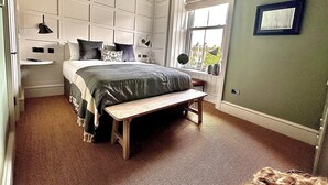 A bedroom with a large bed, a bench, a desk, and a window with a view. - Sugar Boat (Helensburgh)