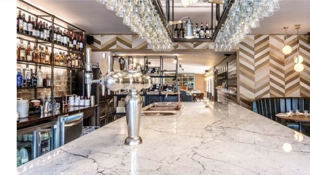 A bar area with a marble countertop, shelves of liquor bottles, and a modern chandelier. - Sugar Boat (Helensburgh)