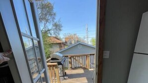 Une vue à travers une porte donnant sur une cour arrière avec une terrasse en bois, une petite maison et un ciel dégagé.