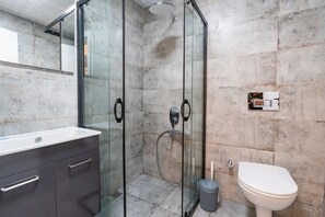 A modern bathroom with a glass-enclosed shower, a toilet, and a vanity with drawers. - Tayla Suit (Kas)
