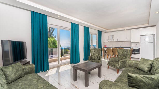 Un salon moderne avec des canapés verts, une table basse et un téléviseur. Il y a un balcon avec vue sur la mer.