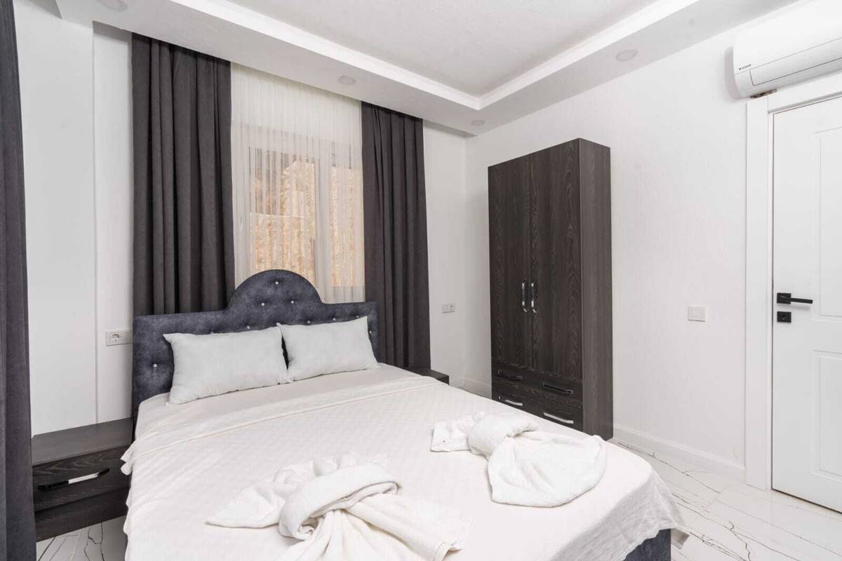 A hotel room with a bed, a wardrobe, a door, and an air conditioning unit.