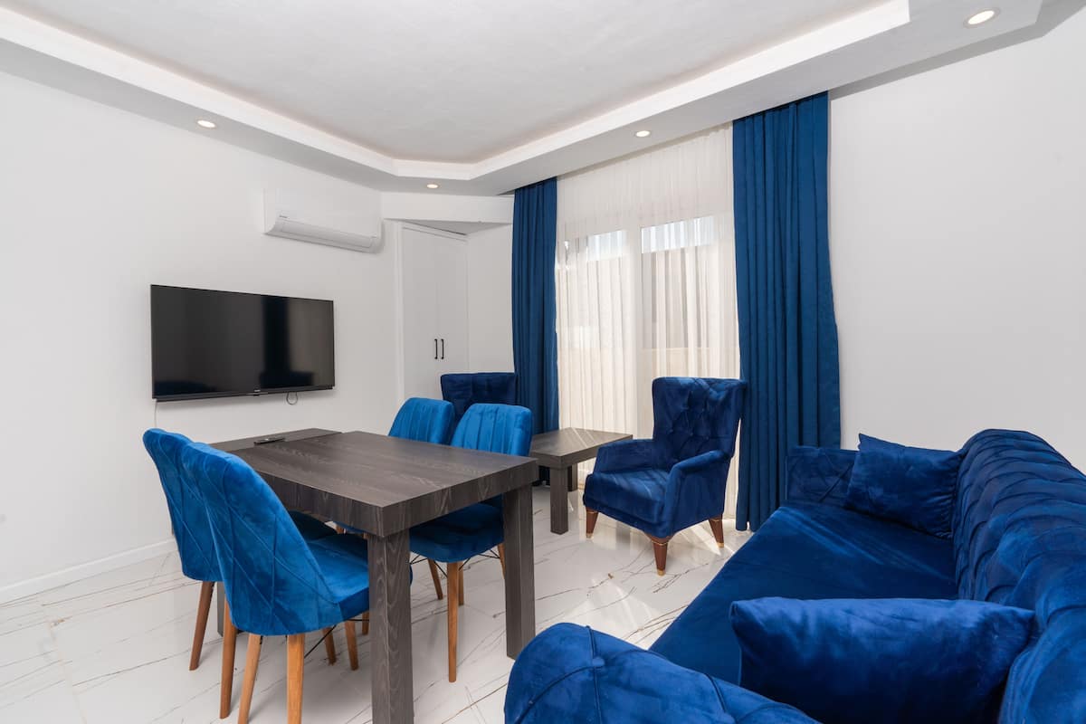 A modern living room with a dark wooden dining table, blue velvet chairs, and a blue sofa.