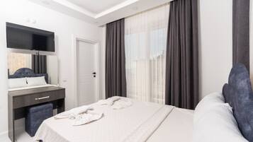 Een moderne hotelkamer met een groot bed, een bureau met stoel, een flatscreen televisie en een groot raam met gordijnen.