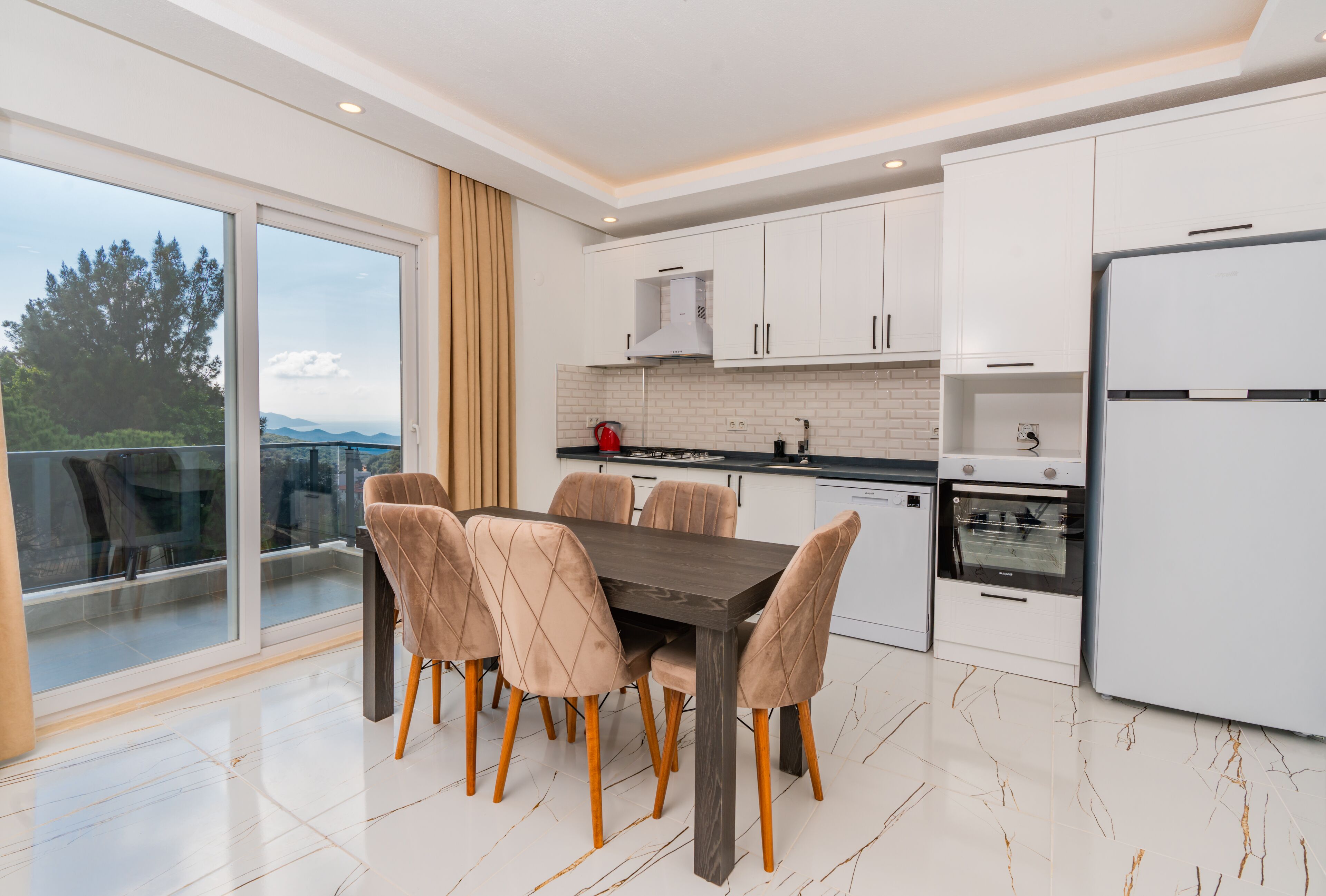 Een moderne keuken met witte kastjes, een donker houten tafel en zes stoelen.