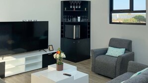 A modern living room with a flat-screen TV, a black entertainment unit with shelves, a white coffee table, and grey sofas. - Pisco Villa: Private Pool & Games on 1400m² (Pisco)