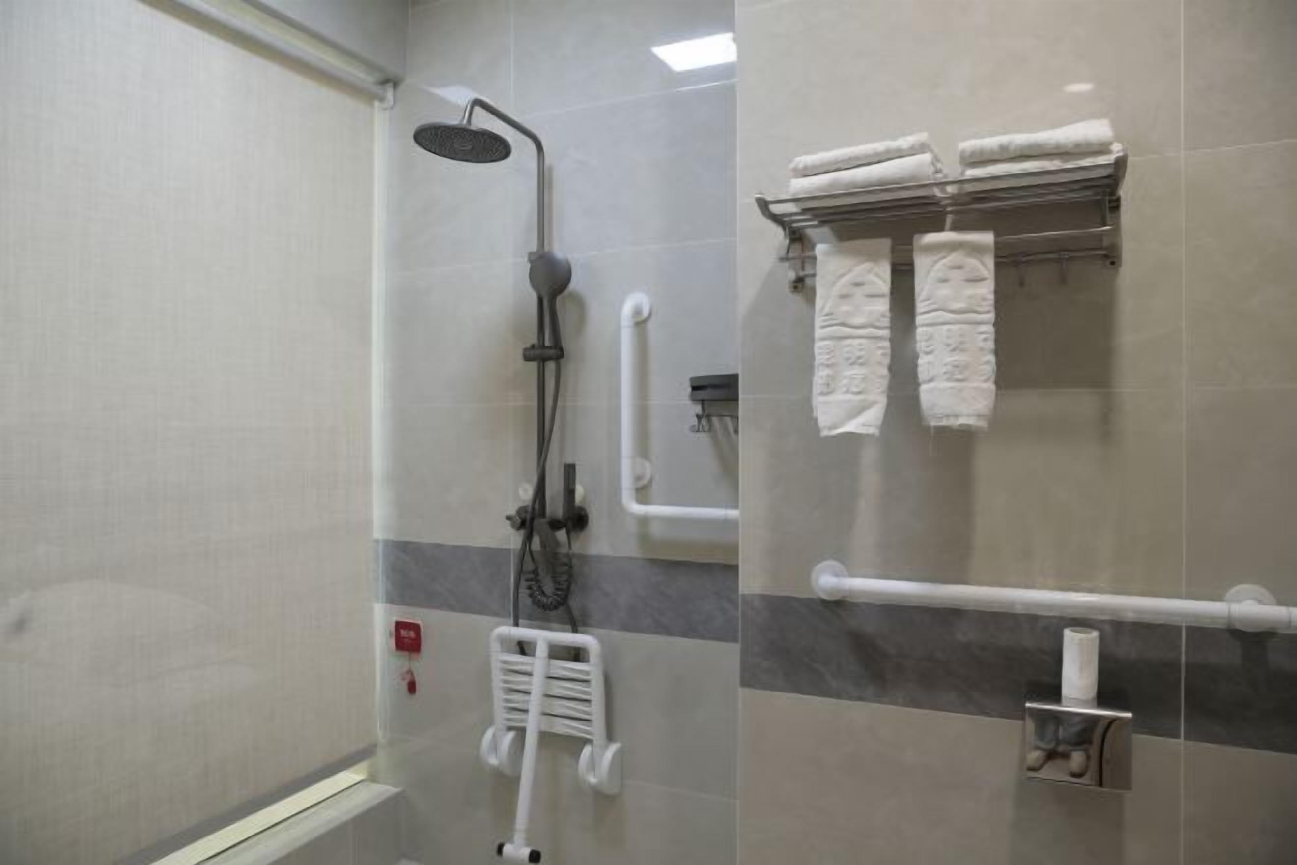 A modern bathroom with a shower, grab bars, a towel rack, and a toilet paper holder.