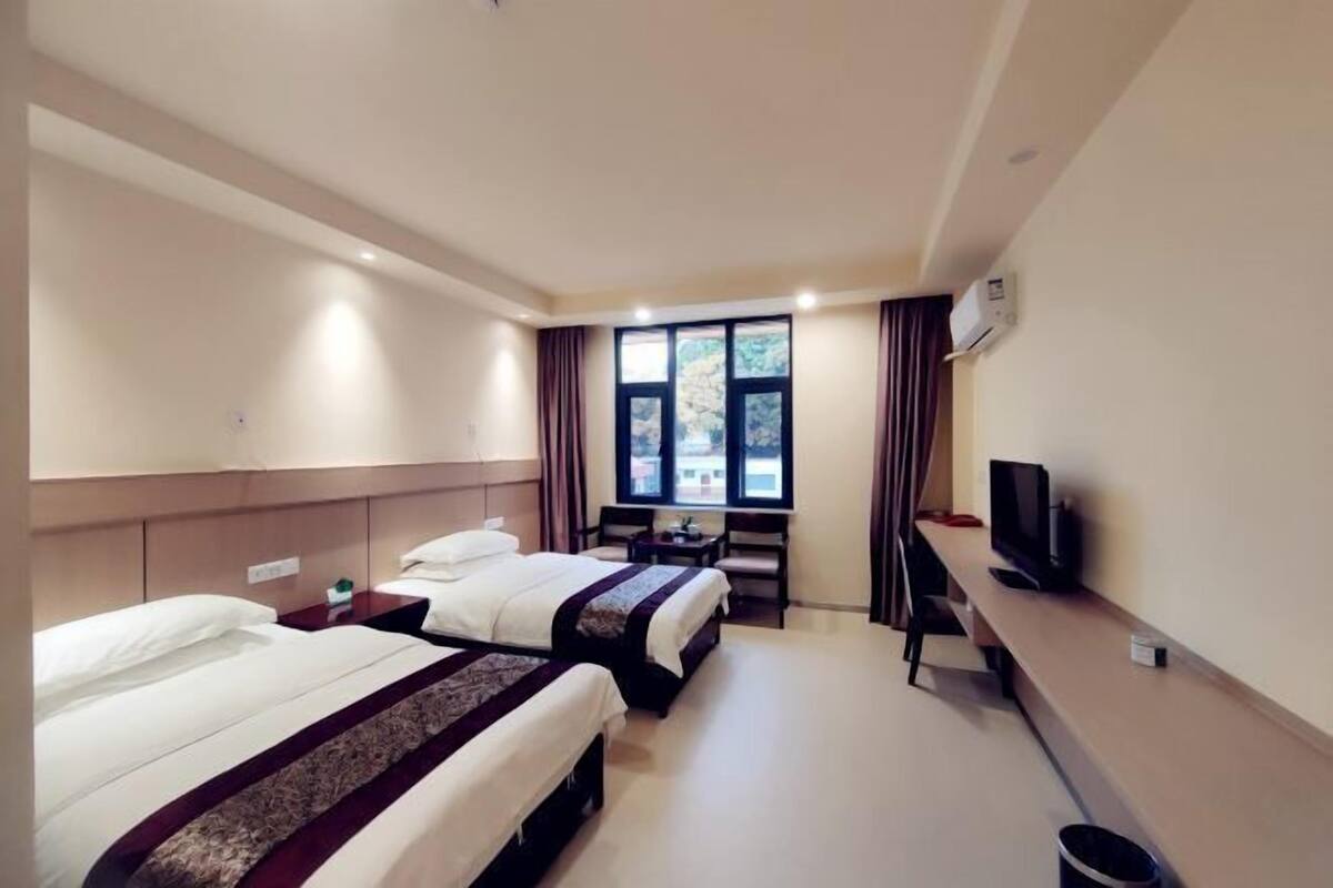 A hotel room with two beds, a desk, a television, and a window with curtains.
