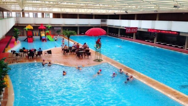 An indoor swimming pool with a slide, a red umbrella, and a seating area with tables and chairs. - Mengshiyuan Hot Spring Resort (Anning)