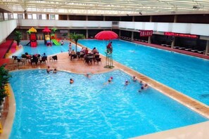 An indoor swimming pool with a slide, a red umbrella, and a seating area with tables and chairs. - Mengshiyuan Hot Spring Resort (Anning)