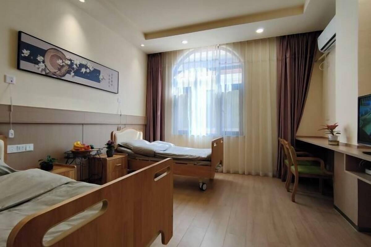 A hotel room with two beds, a desk, a chair, a TV, and a large window with curtains.