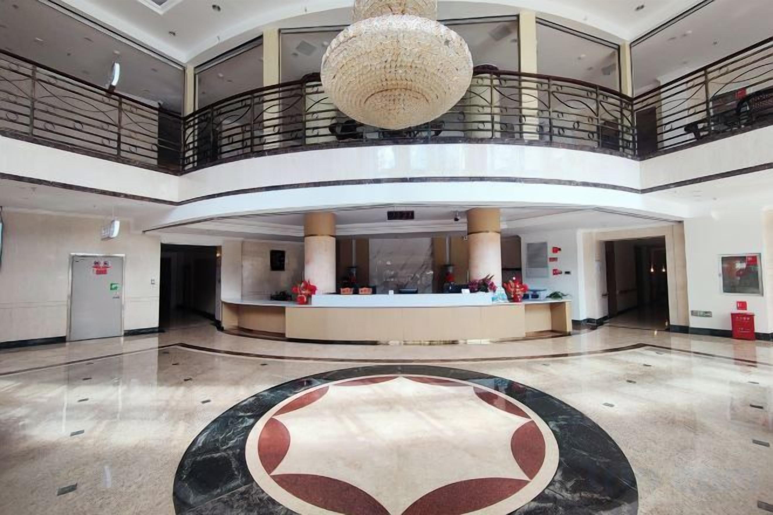 A hotel lobby with a reception desk, a chandelier, and a circular marble design on the floor.