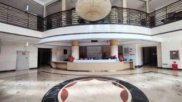 A hotel lobby with a reception desk, a chandelier, and a circular marble design on the floor.