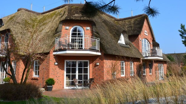 A traditional red brick house with a thatched roof and a balcony.