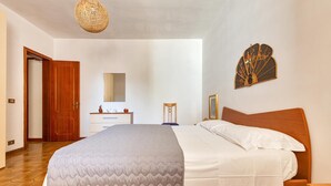 Ein Schlafzimmer mit Bett, Holz-Kopfstück, Nachttisch, Kommode, Spiegel und einer Tür.