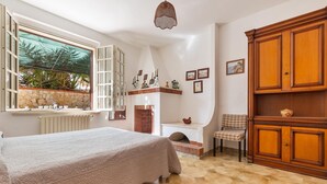 A bedroom with a bed, a window with a view of palm trees, a fireplace, and a wooden cabinet.
