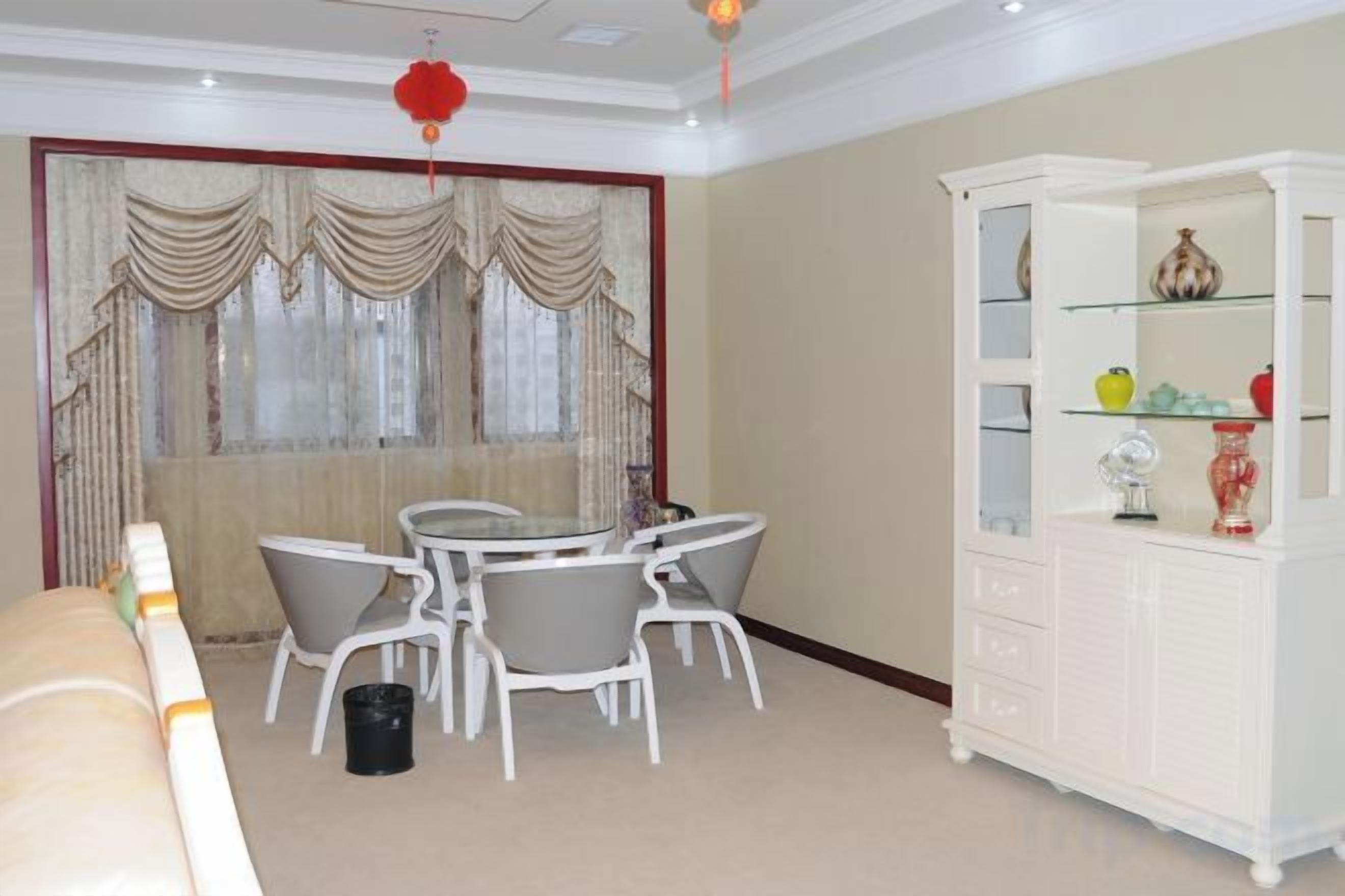 Una habitación con una mesa de comedor y sillas, un armario blanco con puertas de cristal y una ventana con cortinas.
