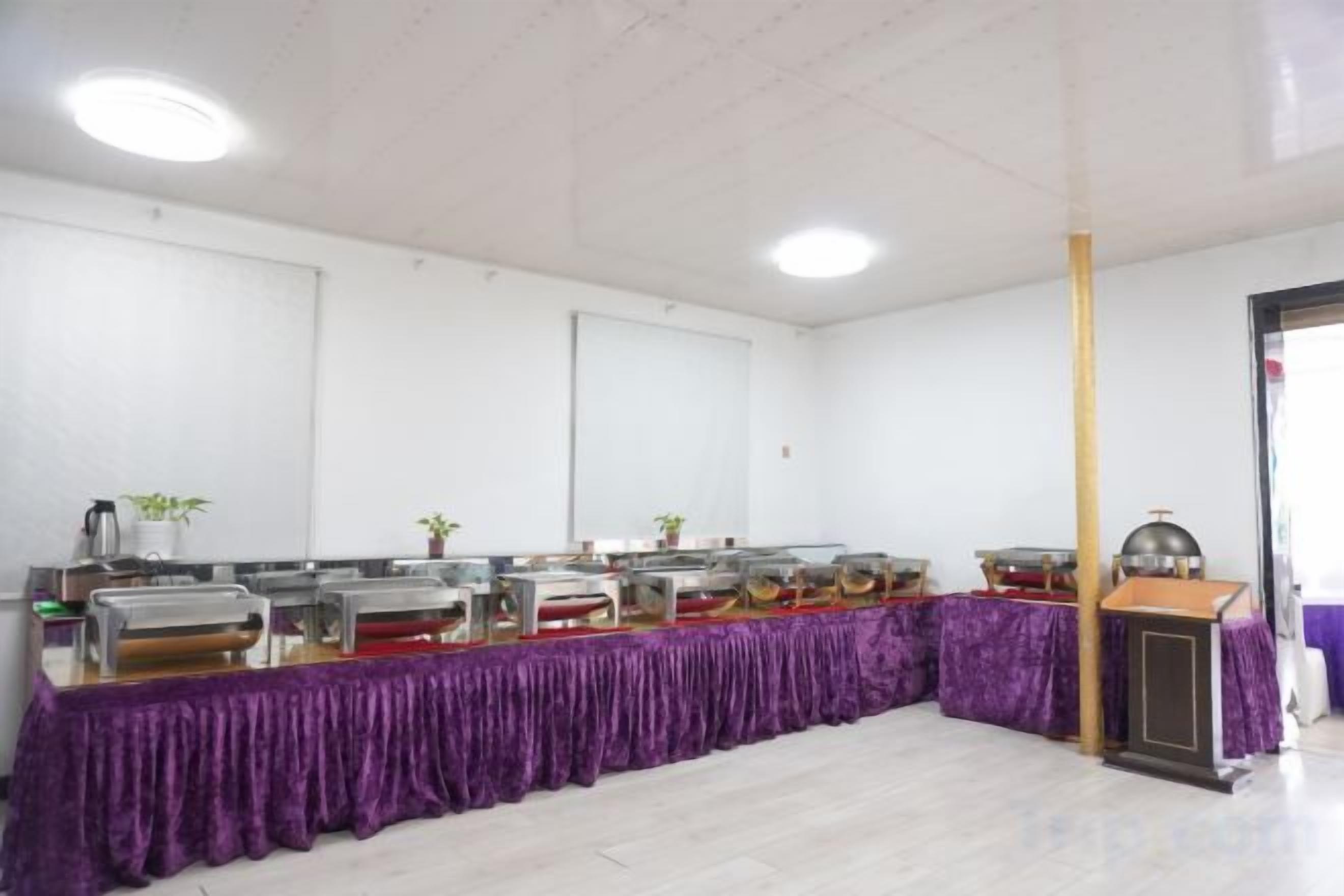 Un'area buffet con diverse postazioni di servizio, una tovaglia viola e un soffitto bianco con faretti.