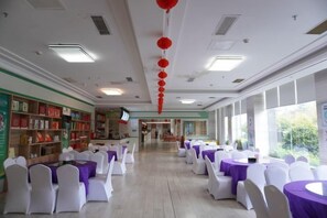Un salón amplio con filas de mesas y sillas, un largo pasillo y ventanas grandes.