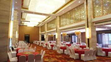A banquet hall with round tables, white chairs, and red tablecloths.