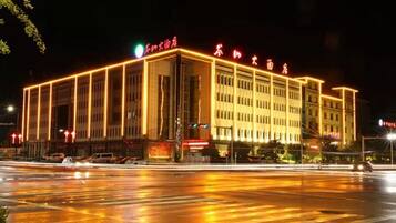 Un edificio de varios pisos con señalización iluminada, una entrada amplia y un paso de cebra enfrente.