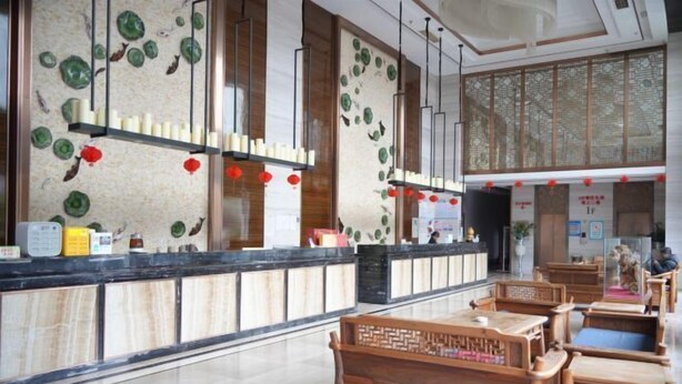 A reception area with a wooden bench, a reception desk, and a wall with decorative elements. - Censhan Hotel (Hengfeng)