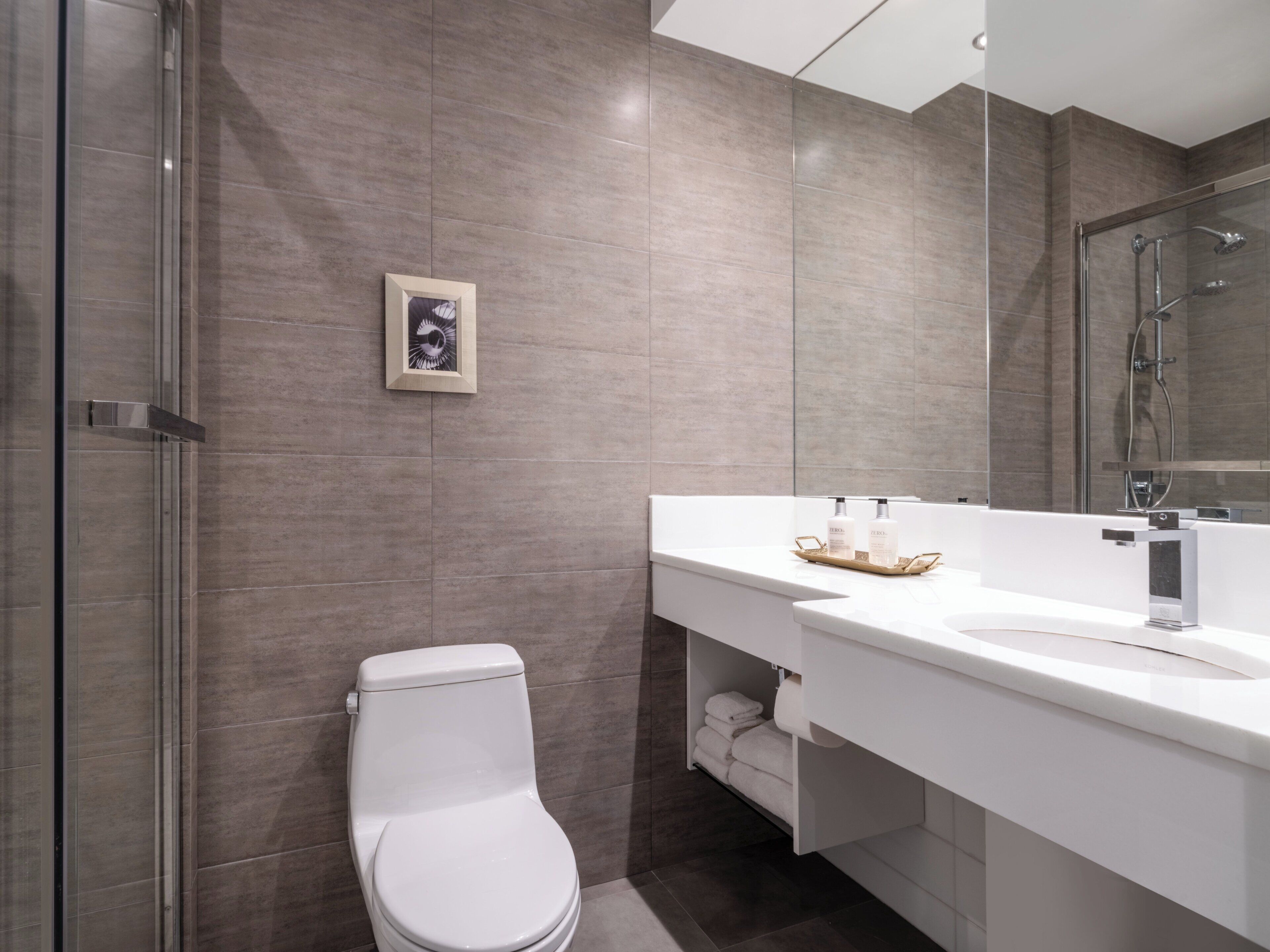 Un bagno moderno con box doccia in vetro, un water bianco e un mobile lavabo con specchio e due flaconi di shampoo.